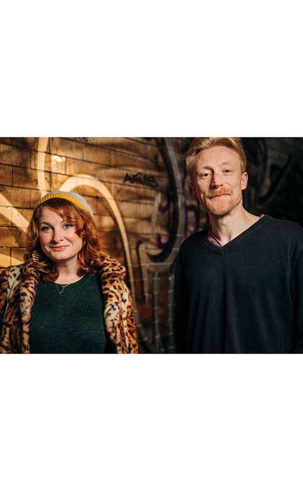 Image of a white mand and woman smiling, the woman has long curly ginger hair and the man is tall with short ginger hair and a beard.